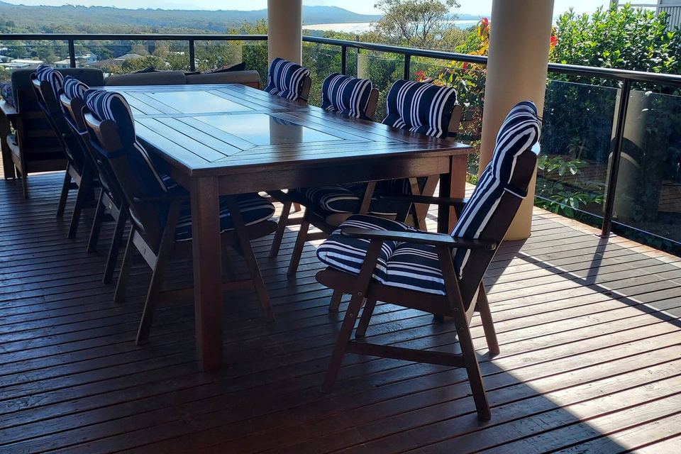 Breakfast table on the deck with striped cushions, bushland beyond the glass rail