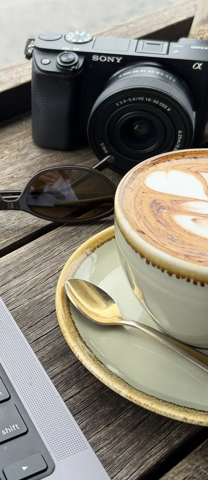 A flat white, sunglasses and a camera on the timber deck table