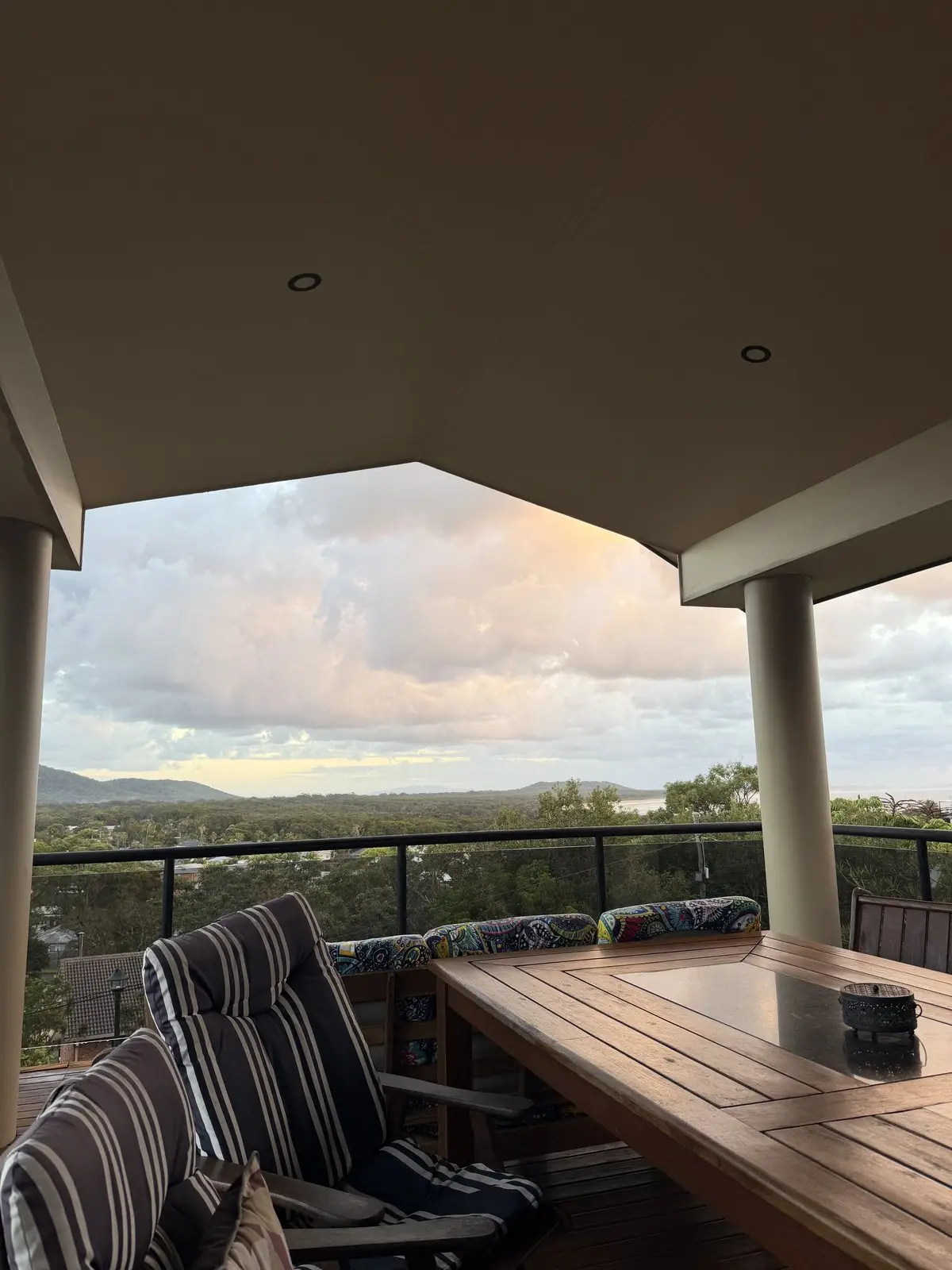 The covered deck at dusk: striped chairs, the long table and pink cloud over the hills