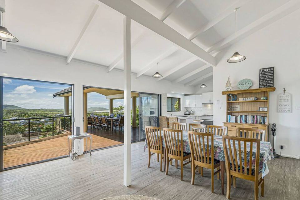 Indoor dining table with timber chairs, the kitchen and a bookshelf behind